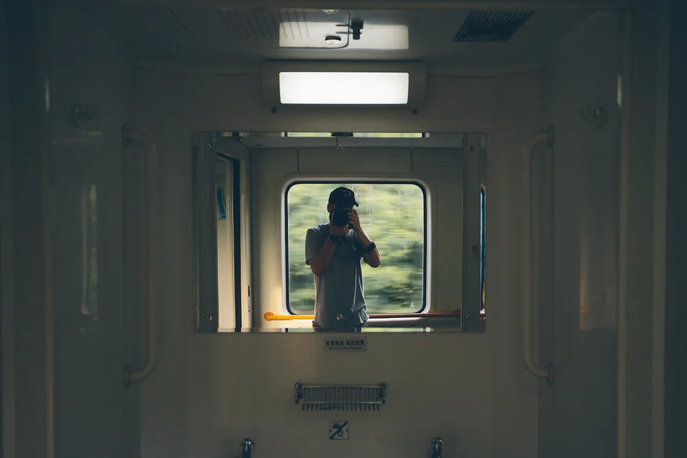 Allen holding a camera, reflected in a train window